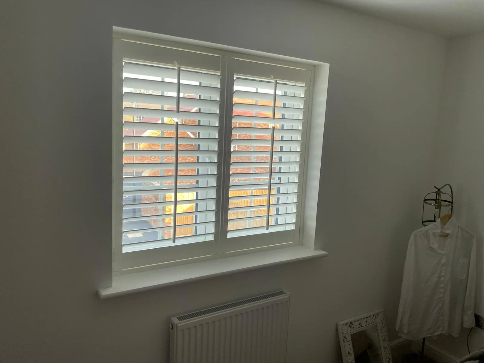 White plantation shutters with open louvres on a bedroom window above a radiator