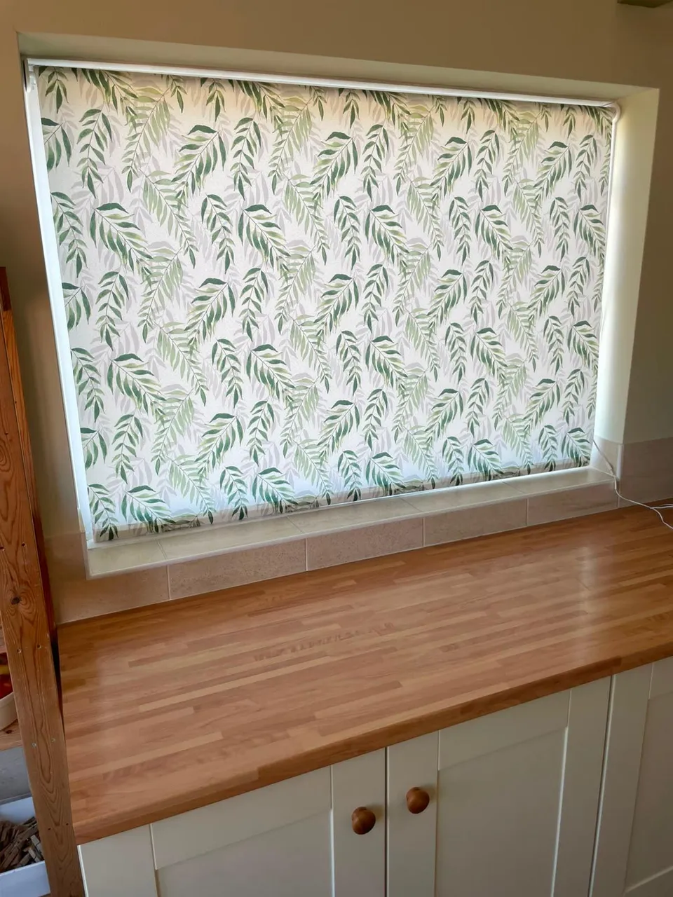 Leaf-print roller blind above a wooden worktop and cream cupboards in a kitchen