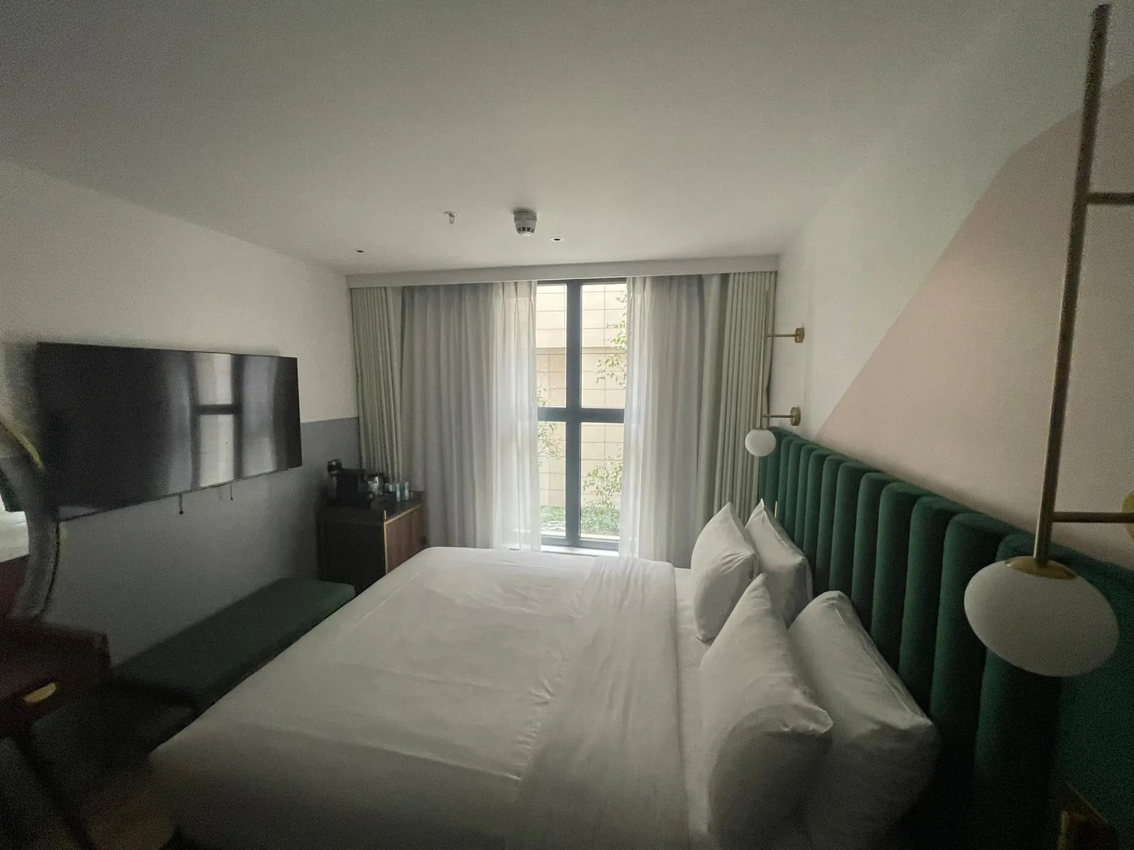 Grey curtains and sheers at a tall window in a hotel bedroom with a wall-mounted TV