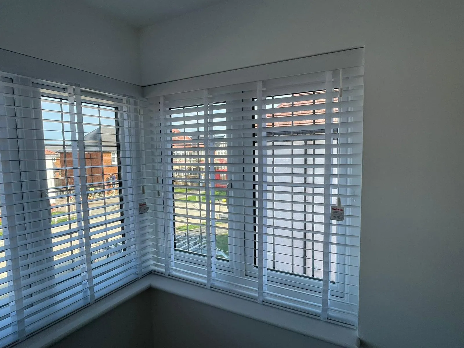 White wooden venetian blinds on a corner window overlooking neighbouring houses
