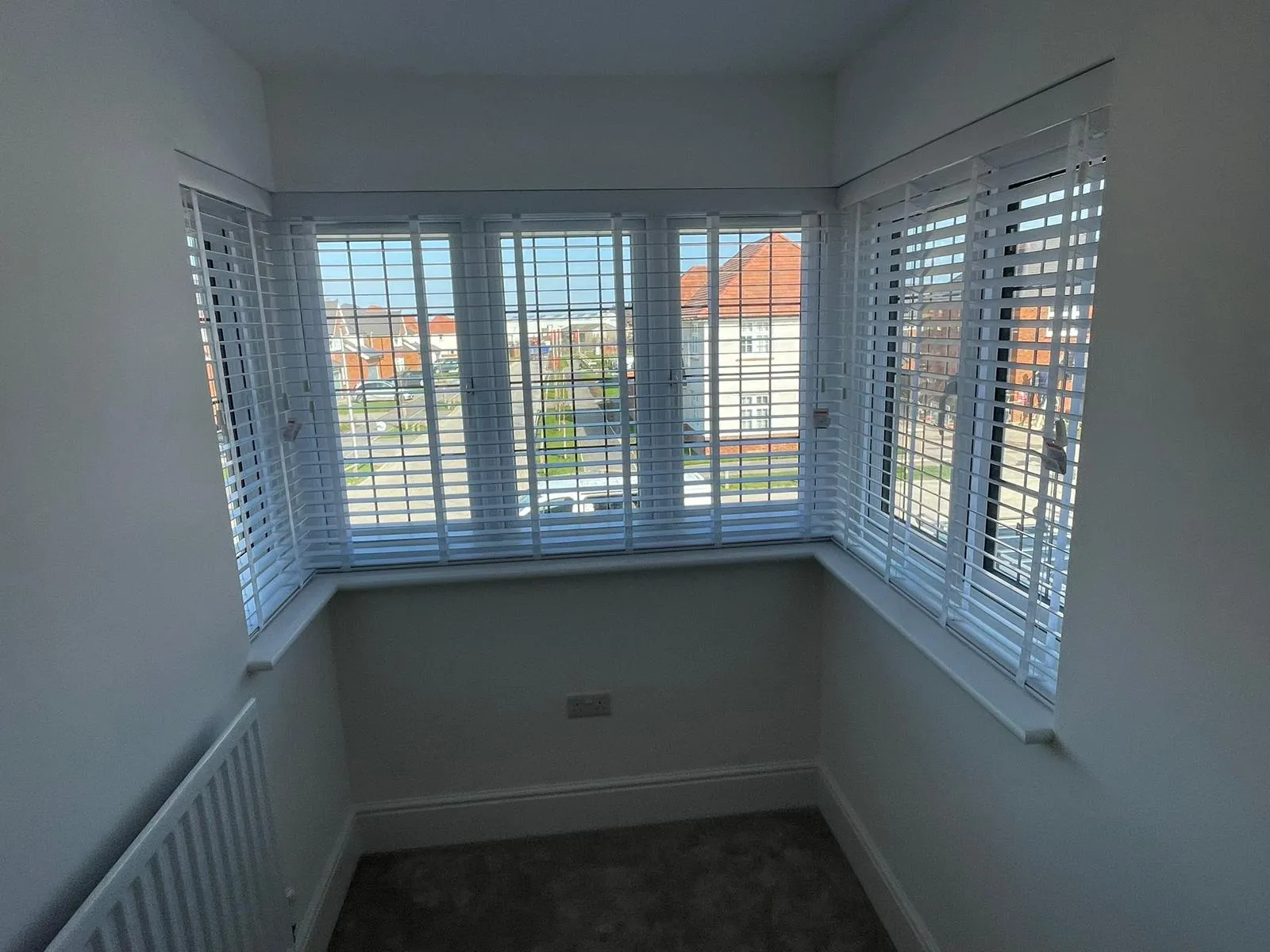 White wooden venetian blinds on a sunny corner bay window in an empty bedroom