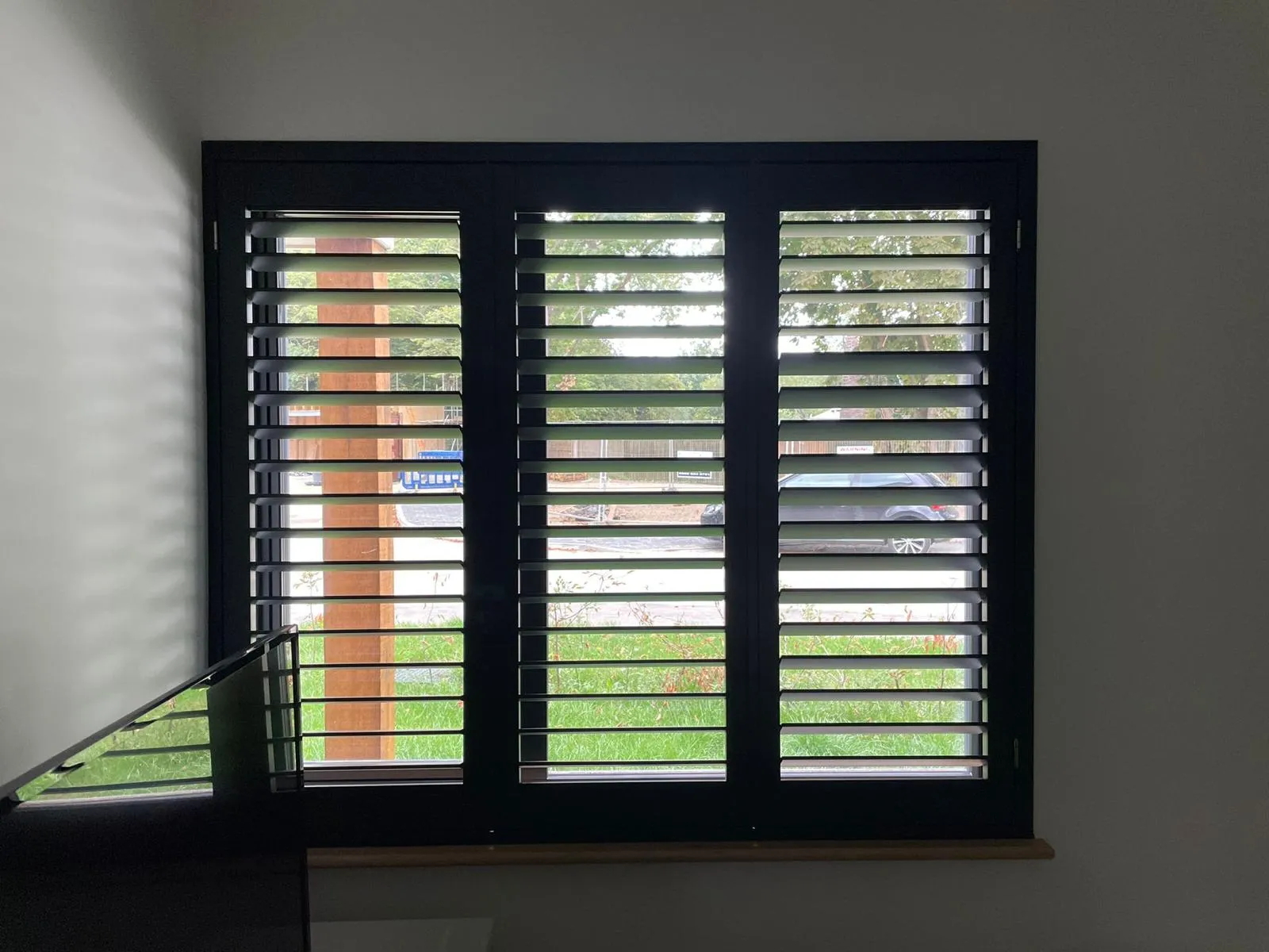 Dark-framed plantation shutters with open louvres on a landing window overlooking the garden