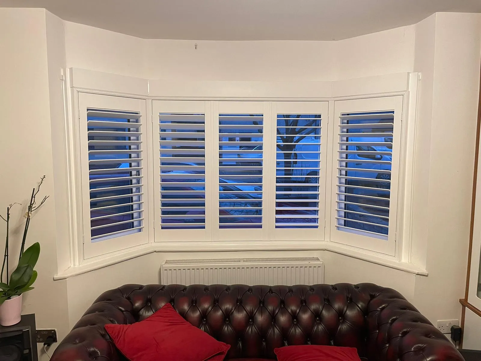 White plantation shutters across a curved bay window behind a leather chesterfield sofa